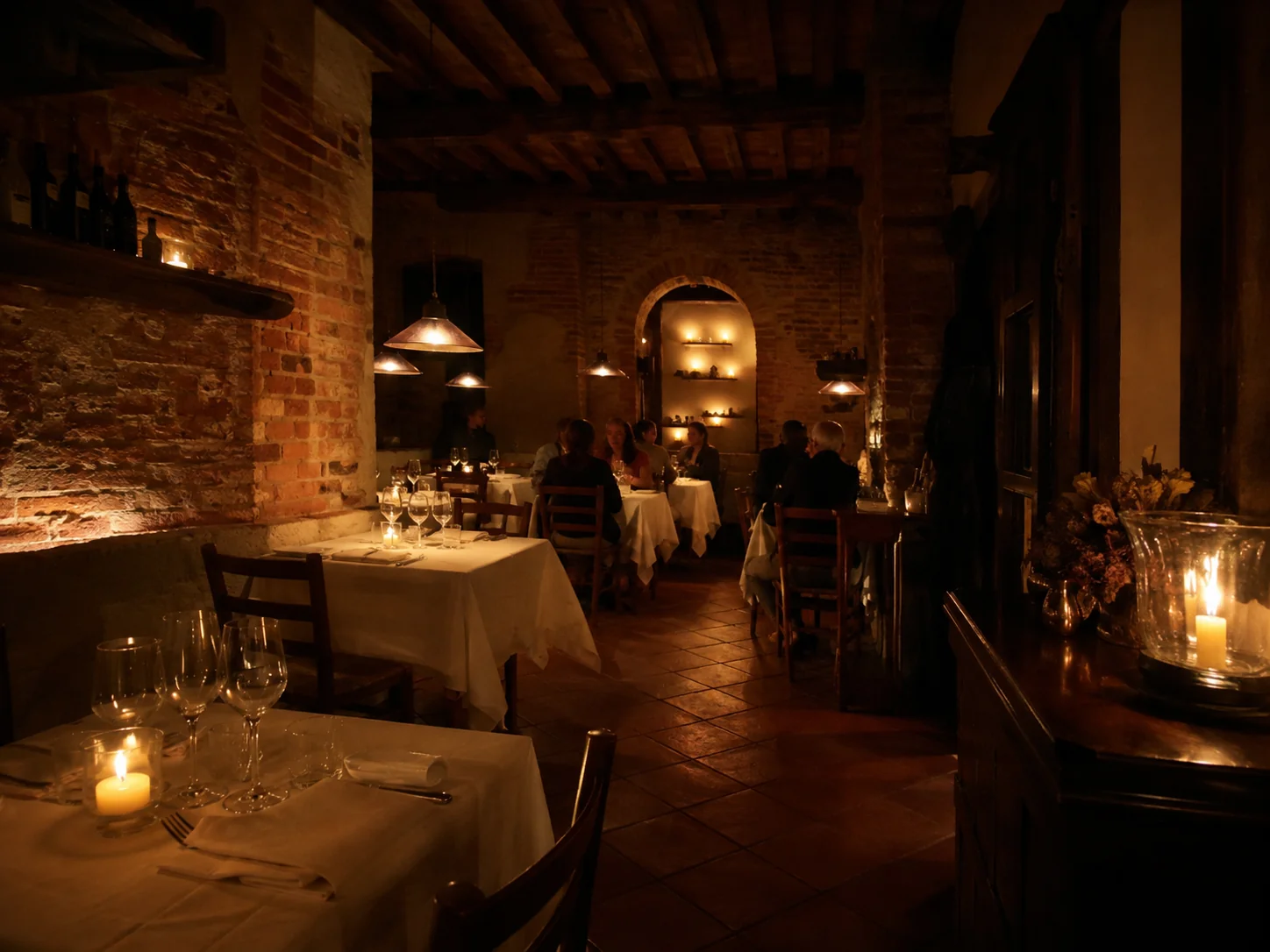 Candlelit dining room at Locanda, brick walls and wood beams, tables set with white linen and glowing candles