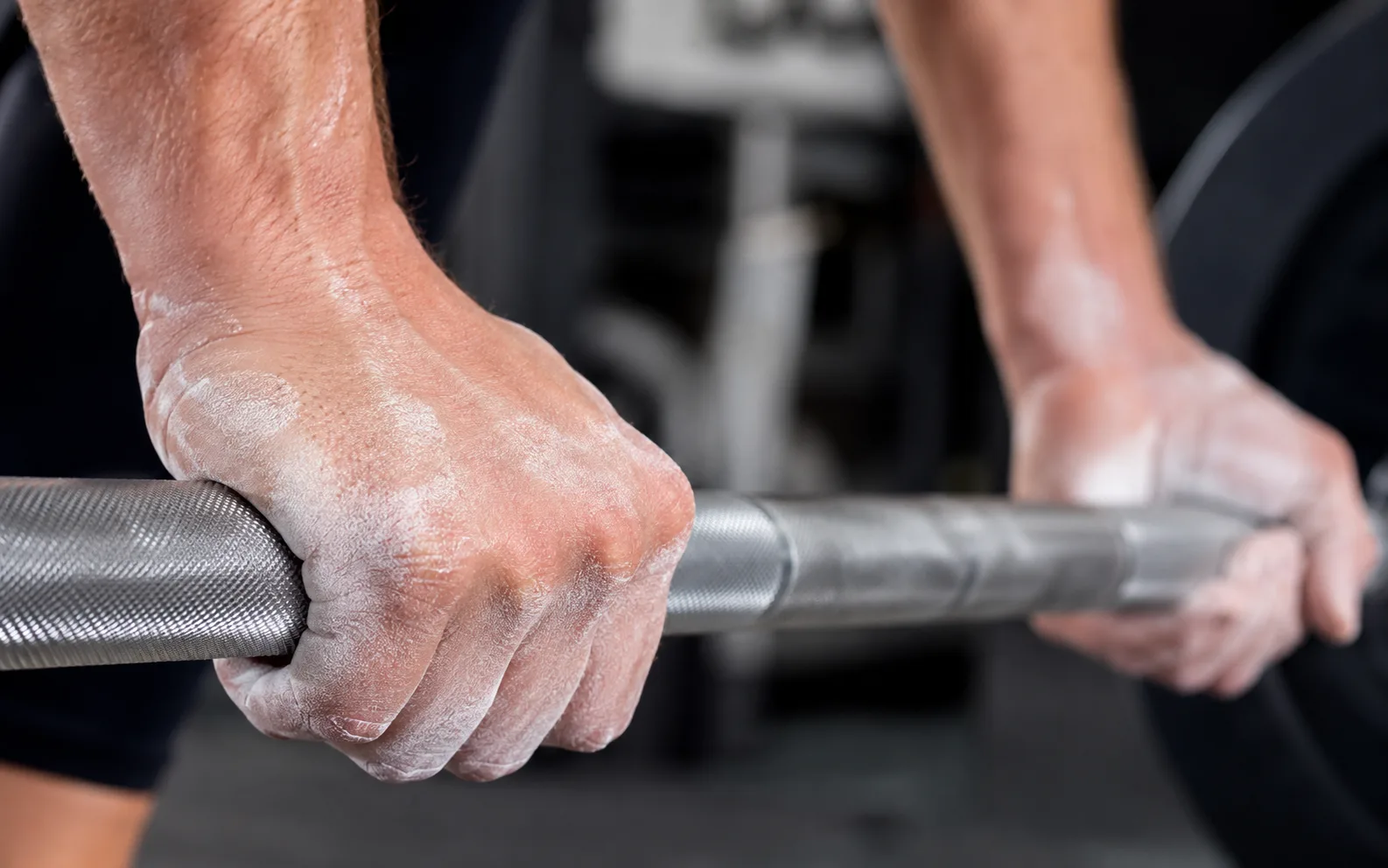Close-up of chalked hands gripping a barbell mid-lift