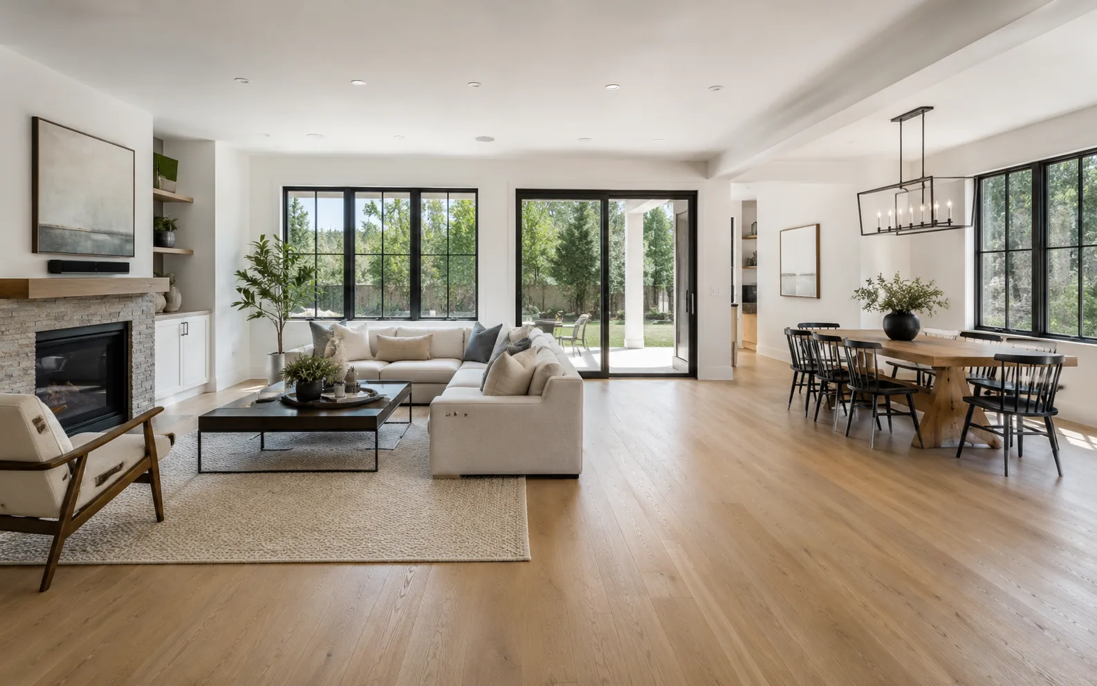 Finished open-concept living and dining space with a stone fireplace, wood flooring, and large windows